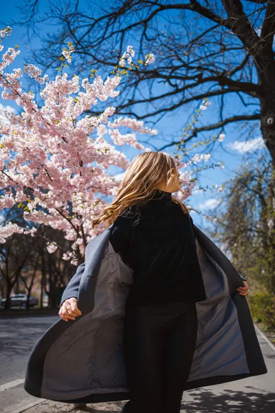 桜の枝が街中の木に花を咲かせます 桜が咲く通りを回転する幸せな女性の女の子 ゴージャスファッショナブルな女の子の屋外 桜の花 — ストック写真