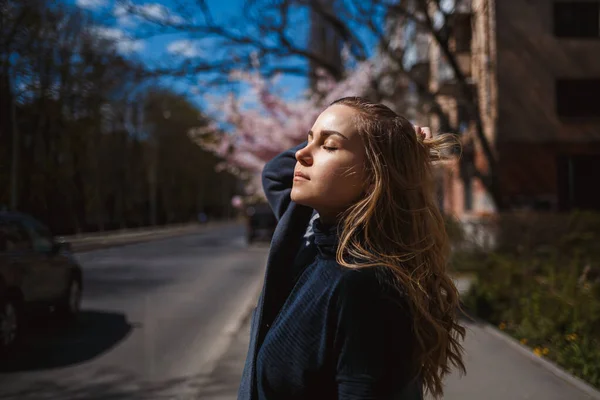 Sakura branches with flowers on a tree on the city streets. Happy woman girl spinning on the street with blooming sakura. Gorgeous fashionable girl outdoors. Sakura tree blossoms.