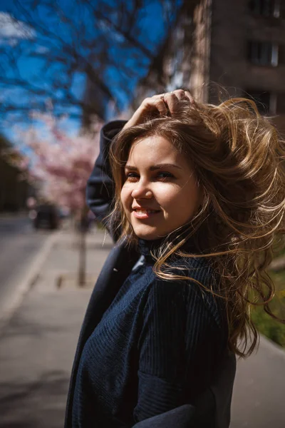 Sakura branches with flowers on a tree on the city streets. Stylish woman girl runs on the street with blooming sakura. Gorgeous fashionable girl outdoors. Sakura tree blossoms.