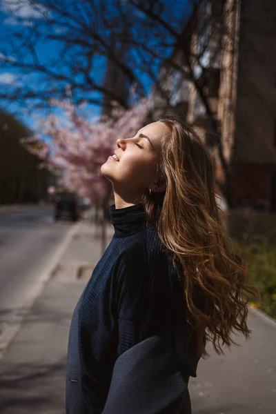 桜の枝が街中の木に花を咲かせます 桜が咲く通りをスタイリッシュな女の子が走っています ゴージャスファッショナブルな女の子の屋外 桜の花 — ストック写真