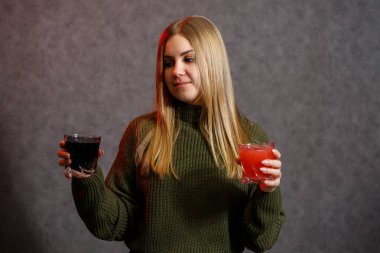 Kız yeşil bir kazak giymişti ve elinde kırmızı ve siyah bir sıvı tutuyordu..