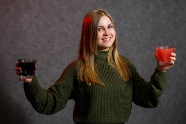 Kız yeşil bir kazak giymişti ve elinde kırmızı ve siyah bir sıvı tutuyordu..