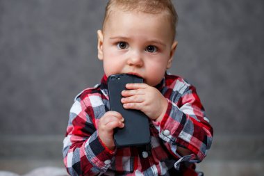 Gömlekli küçük çocuk cep telefonunu kemiriyor.