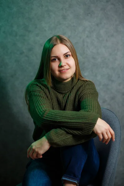 Chica Suéter Verde Jeans Una Silla Gris Sonriendo —  Fotos de Stock