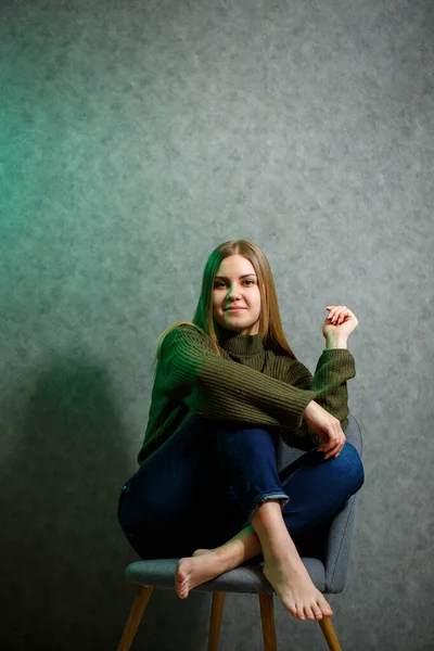 Chica Suéter Verde Jeans Una Silla Gris Sonriendo —  Fotos de Stock