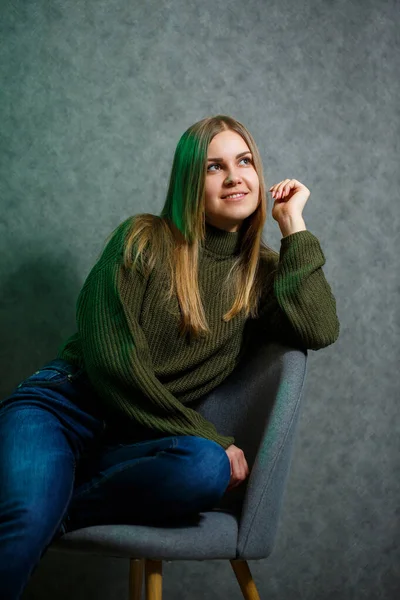 女の子で緑のセーターとジーンズでグレーの椅子と笑顔 — ストック写真