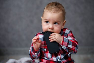 Gömlekli küçük çocuk cep telefonunu kemiriyor.