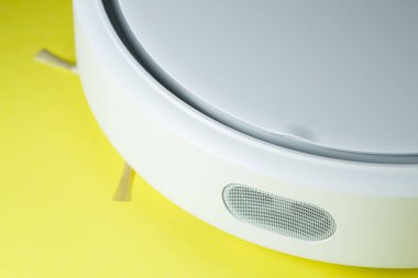 Beyaz robot temizleyicisi sarı arka planda evi temizliyor.
