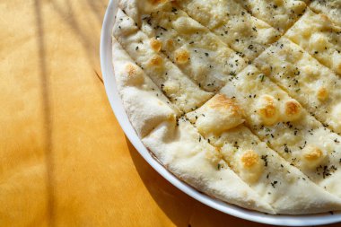 Parlak güneş ışığı altında üzerine peynir serpiştirilmiş baharatlı büyük taze pizza.