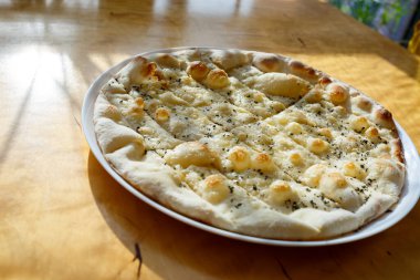 Parlak güneş ışığı altında üzerine peynir serpiştirilmiş baharatlı büyük taze pizza.