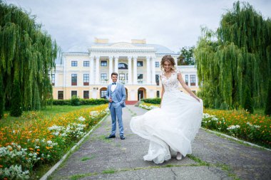 Damat ve gelin kostümü içinde genç şık bir adam. Düğün günlerinde parkta tren yürüyüşü yapan beyaz elbiseli güzel bir kız.