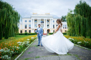Damat ve gelin kostümü içinde genç şık bir adam. Düğün günlerinde parkta tren yürüyüşü yapan beyaz elbiseli güzel bir kız.