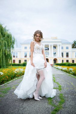 Beyaz elbiseli, trenli ve yürüyüşlü güzel bir gelin düğün günlerinde büyük bir evin arka planına döndü.