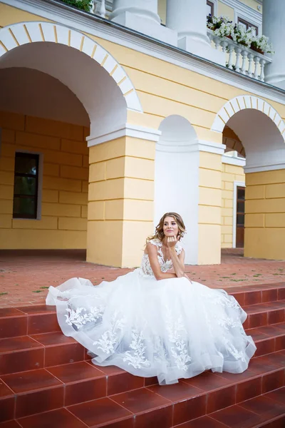 結婚式の日に柱のある大きな家の裏を電車が歩いている白いドレスを着た美しい女の子の花嫁 — ストック写真