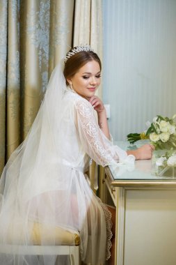 Gelin beyaz önlüklü ve peçeli makyaj masasında oturuyor.