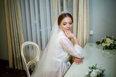 Gelin beyaz önlüklü ve peçeli makyaj masasında oturuyor.