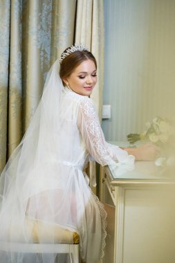 Gelin beyaz önlüklü ve peçeli makyaj masasında oturuyor.