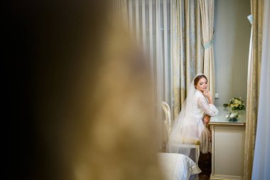 Gelin beyaz önlüklü ve peçeli makyaj masasında oturuyor.