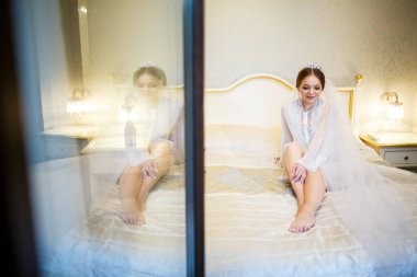 Gelin, beyaz önlüklü, düğün sabahı yatağında.