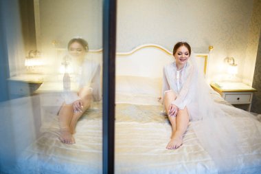 Gelin, beyaz önlüklü, düğün sabahı yatağında.