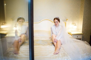 Gelin, beyaz önlüklü, düğün sabahı yatağında.