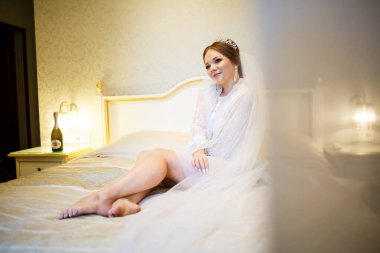 Gelin, beyaz önlüklü, düğün sabahı yatağında.