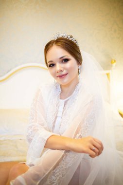 Gelin, beyaz önlüklü, düğün sabahı yatağında.