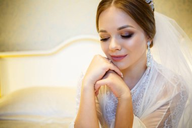 Gelin, beyaz önlüklü, düğün sabahı yatağında.