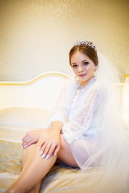 Gelin, beyaz önlüklü, düğün sabahı yatağında.