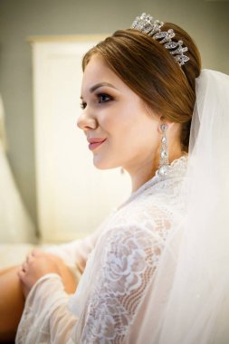 Gelin, beyaz önlüklü, düğün sabahı yatağında.