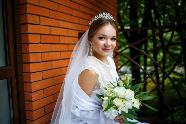 Duvak takmış güzel bir gelin ve elinde bir buketle bir battaniyenin üzerinde oturan beyaz bir ceket.