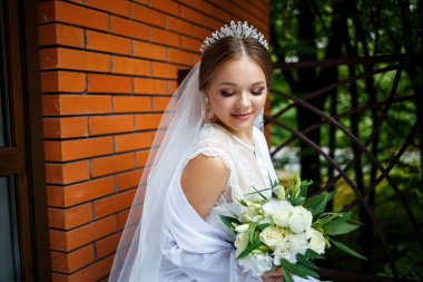 Duvak takmış güzel bir gelin ve elinde bir buketle bir battaniyenin üzerinde oturan beyaz bir ceket.