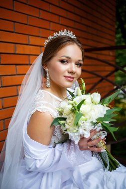 Duvak takmış güzel bir gelin ve elinde bir buketle bir battaniyenin üzerinde oturan beyaz bir ceket.