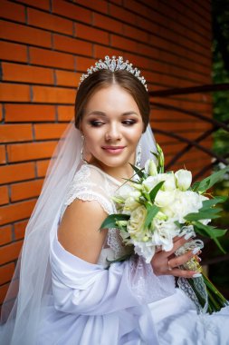 Duvak takmış güzel bir gelin ve elinde bir buketle bir battaniyenin üzerinde oturan beyaz bir ceket.