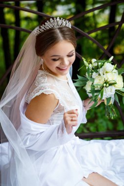 Duvak takmış güzel bir gelin ve elinde bir buketle bir battaniyenin üzerinde oturan beyaz bir ceket.