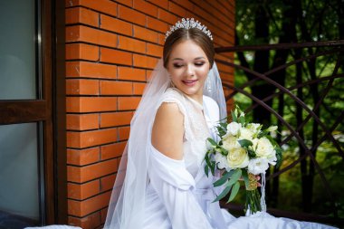 Duvak takmış güzel bir gelin ve elinde bir buketle bir battaniyenin üzerinde oturan beyaz bir ceket.