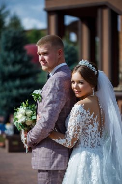 Beyaz gelinlik içinde gelin ve büyük adımlı tuğla bir binanın arka planında damat.