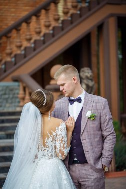 Beyaz gelinlik içinde gelin ve büyük adımlı tuğla bir binanın arka planında damat.