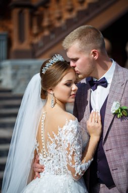 Beyaz gelinlik içinde gelin ve büyük adımlı tuğla bir binanın arka planında damat.