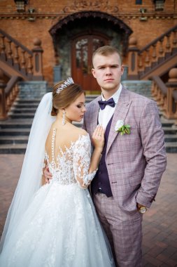 Beyaz gelinlik içinde gelin ve büyük adımlı tuğla bir binanın arka planında damat.