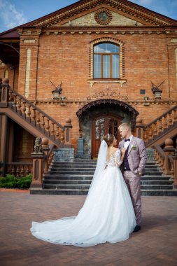 Beyaz gelinlik içinde gelin ve büyük adımlı tuğla bir binanın arka planında damat.