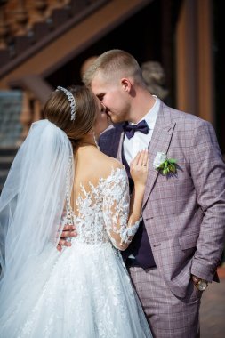 Beyaz gelinlik içinde gelin ve büyük adımlı tuğla bir binanın arka planında damat.