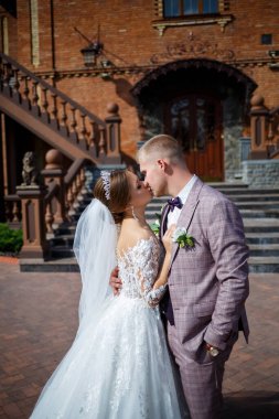 Beyaz gelinlik içinde gelin ve büyük adımlı tuğla bir binanın arka planında damat.