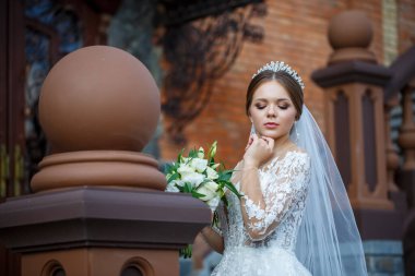 Beyaz elbiseli gelin ellerinde buket ve kafasında taçla.