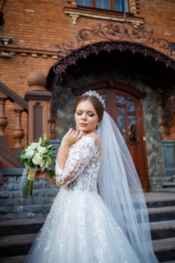 Beyaz elbiseli gelin ellerinde buket ve kafasında taçla.