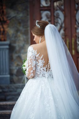 Beyaz elbiseli gelin ellerinde buket ve kafasında taçla.