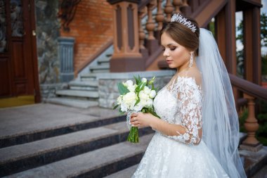 Beyaz elbiseli gelin ellerinde buket ve kafasında taçla.