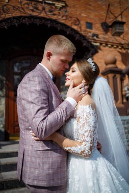 Beyaz gelinlik içinde gelin ve büyük adımlı tuğla bir binanın arka planında damat.