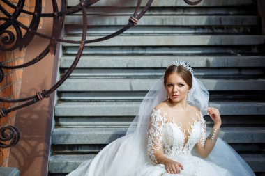 Beyaz gelinlikli güzel gelin merdivenlerde oturur ve güzel bir şekilde gülümser.