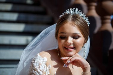 Beyaz gelinlikli güzel gelin merdivenlerde oturur ve güzel bir şekilde gülümser.